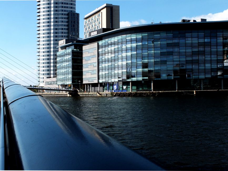 A view of the residential apartments along Heron Quays on the Isle of Dogs, with modern multi-story buildings constructed from beige brick and glass facades. The buildings are positioned on either sid